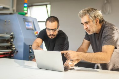 İki saha bakım mühendisi teknisyeni elektirikçi dizüstü bilgisayarlı makine donanım ve yazılım sistemini denetleyip kontrol ediyor. Elektrik kurulumu