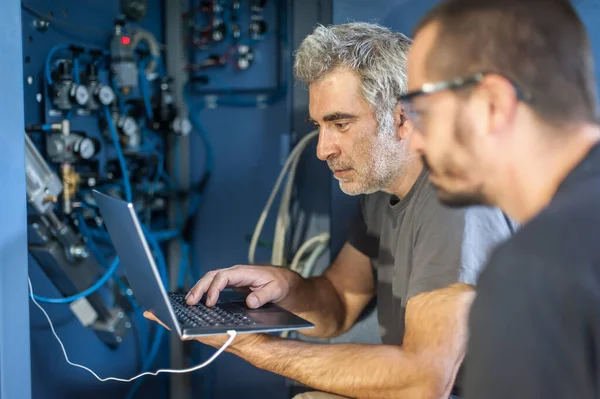 Two field service maintenance engineer technician electrician inspect and control machine hardware and software system with laptop computer. Electric installation