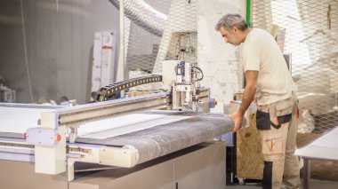 Fabrika işçi teknisyeni, kumaş tekstil malzemelerini kesmek için CNC dijital kesici makinesinde çalışıyor.