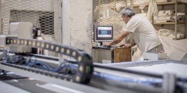 Fabrika işçi teknisyeni, kumaş tekstil malzemelerini kesmek için CNC dijital kesici makinesinde çalışıyor.