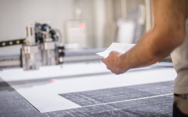 Fabrika işçi teknisyeni, kumaş tekstil malzemelerini kesmek için CNC dijital kesici makinesinde çalışıyor.