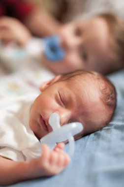 İki kardeş yumuşak bir yüzeyde birlikte uyur, hassas bir an yaşarlar. Ağabeyi arka planda usulca dinlenirken yeni doğan ön planda huzur içinde rüya görür..