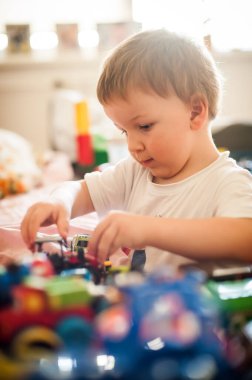 Küçük bir çocuk ışık ve oyuncaklarla dolu canlı bir odada çeşitli renkli oyuncak arabalarla oynamaya konsantre olur..