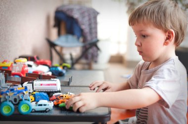Parlak bir odada, genç bir çocuk masaya odaklanmış, çeşitli oyuncak arabaları düzenliyor. Detaylara olan ilgisi yaratıcı oyun ve yaratıcılığa olan sevgisini gösteriyor..