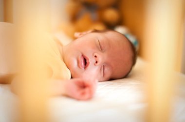 Sıcak bir çocuk odası atmosferiyle çevrili bir beşikte huzur içinde uyuyan bir bebek. Yumuşak güneş ışığı içinden süzülüp huzur dolu bir an yaratıyor..