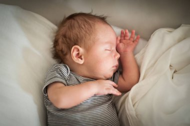 Yeni doğmuş bir bebek sakin bir ifadeyle yumuşak bir yüzeyde dinlenerek mışıl mışıl uyuyor. Yumuşak ışık, erken yaşamın masumiyetini gösteren huzurlu bir atmosfer yaratır..