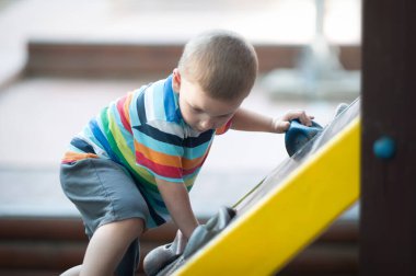 Çizgili tişörtlü genç bir çocuk oyun parkındaki parlak sarı oyun yapısına tırmanıyor. O yükselişine odaklanırken güneş batıyor, dışarıda oyun oynamaktan keyif alıyor..