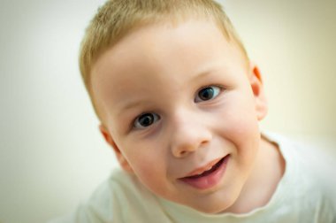 Kısa sarı saçlı genç bir çocuğun kameraya baktığı görülüyor. Hafifçe gülümsüyor, birkaç dişini gösteriyor. Sahne aydınlık ve o içeride..