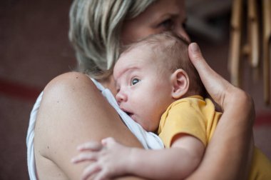 Bir kreş öğretmeni, gün içinde çocuk yuvasında yeni doğan bebeği rahatlatan ve rahatlatan sevimli bir bebeği göğsüne dayar. Bebek uyanık ve huzurlu görünüyor..