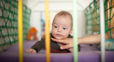 Bir anne bebeğiyle meşgul, bebek yatakta yatarken oynaşıyor ve sarılıyor. Odanın yumuşak bir ışığı ve sıcak bir atmosferi var. Sevgi dolu bir an yaratıyor..