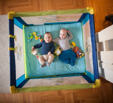 İki sevimli ikiz kardeş, neşeli oyuncaklarla çevrili canlı bir oyun parkında yan yana uzanmış, keyifli bir öğleden sonranın tadını çıkarıyorlar..