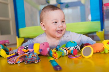 Neşeli bir bebek, güneşli sarı bir yüzeyde canlı bir oyuncak dizisiyle etkileşime girer. Oda neşe saçıyor, keşif ve neşe dolu anlar..