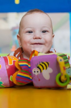 Neşeli bir bebek güneşli bir oyun odasında canlı oyuncaklarla oynarken geniş bir şekilde gülümser. Atmosfer sıcaklıkla, yaratıcılıkla ve çocukluk merakıyla doludur..