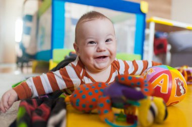 Neşeli bir bebek, canlı oyuncaklarla çevrili yumuşak bir paspasın üzerinde yatıyor. Onun büyük gülüşü neşeyle etrafı aydınlatırken sabah güneşi altında neşeli bir şekilde etrafı keşfediyor..