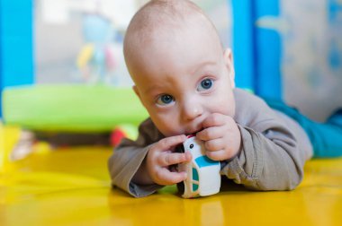 Küçük bir oyuncak araba tarafından büyülenmiş parlak sarı bir paspasın üzerinde bir bebek yatıyor. Oyun alanı canlı renklerle dolu, keşif için mükemmel neşeli bir atmosfer yaratıyor..