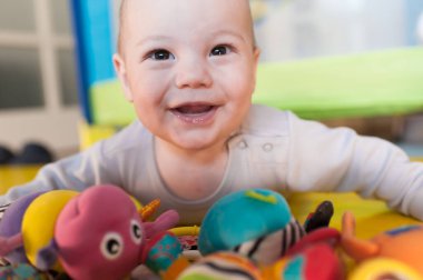 Neşeli bir bebek, rahat bir oyun odasında canlı oyuncakların arasında mutlu bir şekilde emekliyor. Güneş ışığı içeri süzülür, kahkahalarla dolu sıcak ve davetkar bir atmosfer yaratır..