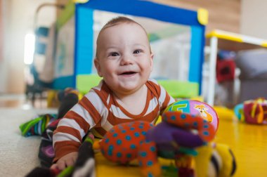 Neşeli bir bebek, parlak bir oyun odasında canlı oyuncaklarla çevrili yumuşak bir paspasın üzerinde oynar. Ufaklık keyifle gülüyor, neşeli bir ruh ve merak sergiliyor..