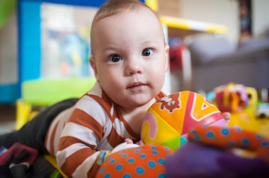 Yumuşak bir oyun hasırının üzerinde, meraklı bir bebek, canlı bir oyun odasında canlı oyuncaklara uzanır. Neşeli atmosfer eğlenceli keşiflere ve öğrenmeye ilham verir..