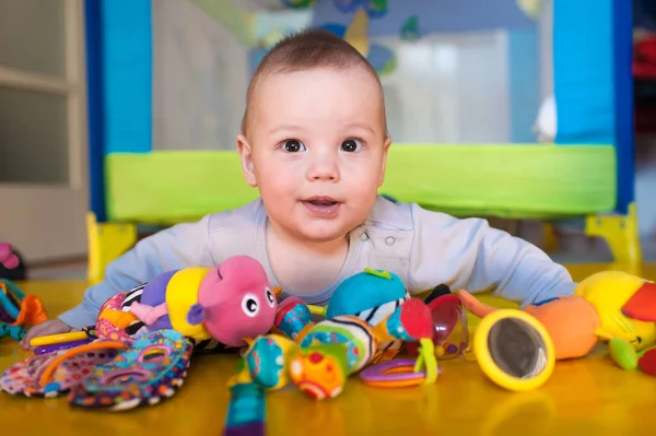 Neşeli bir bebek canlı oyuncaklarla çevrili renkli bir oyun hasırının üzerinde yatıyor. Oda aydınlık, heyecan ve merak dolu bir atmosfer yaratıyor..