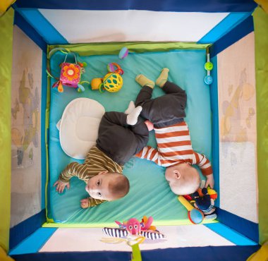 İki ikiz kardeş oyun parkında karınlarının üstünde oyuncaklarla etkileşim halindeler. Birlikte iyi vakit geçiriyorlar. Ayar parlak ve eğlenceli..