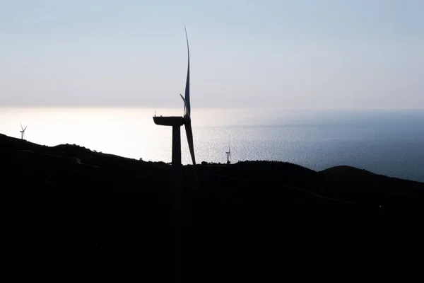 Silhouette of a single wind turbine - Wind electricity power plant - built on mountains from a high point. In the blurred background, a magnificent view of the Aegean Sea is visible.
