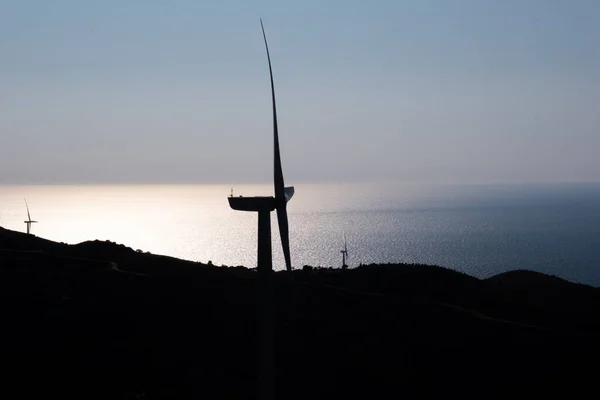 Silhouette of a single wind turbine - Wind electricity power plant - built on mountains from a high point. In the blurred background, a magnificent view of the Aegean Sea is visible.