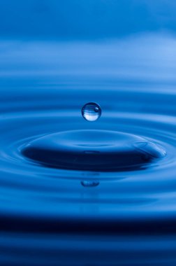 Vertical photo of a blue water drop splash with ripples
