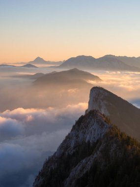 Sonnenaufgang mit Nebelmeer vom Gipfel des Schober am Fuschlsee in Salzburg. Zu sehen sind viele andere Berggipfel, die aus dem Nebel ragen, unter anderem der Traunstein. Avusturya 'da bir dağın tepesinde bulutların üzerinde gün doğumu
