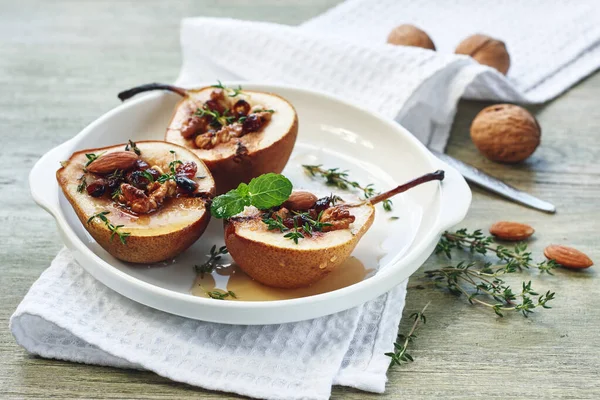 Baked pears with nuts, raisins, honey and cinnamon in a white plate on a green wooden table.