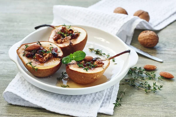 Fındıklı fırında armut, kuru üzüm, bal ve tarçın yeşil ahşap bir masada beyaz bir tabakta.