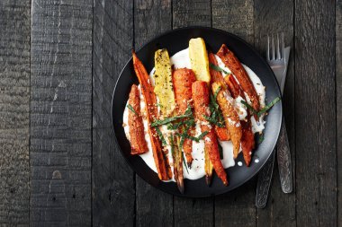 Yoğurtlu kızarmış havuç salatası, baharatlar ve siyah arka planda otlar..
