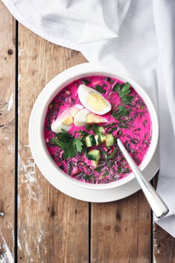 Soğuk pancar çorbası, salatalık, yumurta ve otlar ahşap bir masada..