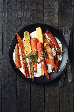Yoğurtlu kızarmış havuç salatası, baharatlar ve siyah arka planda otlar..