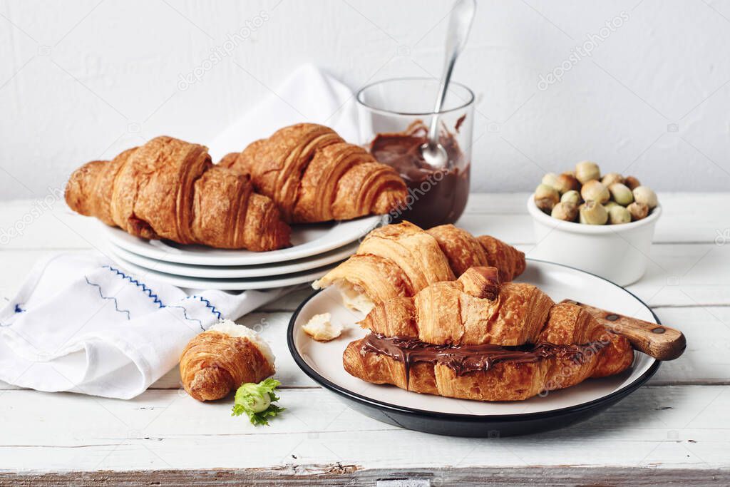 Freshly baked croissants with chocolate cream on a white rustic table.