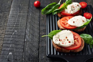 Açık sandviç veya mozzarella peynirli bruschetta, domates ve fesleğen, koyu ahşap arka planda Caprese..