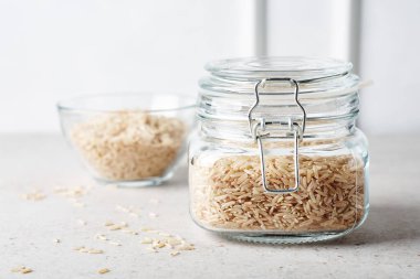 Açık arkaplanda cam bir kavanozda kurumuş kahverengi pirinç..