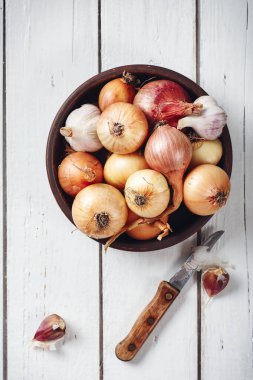 Beyaz ahşap arka planda soğan ve sarımsaklı bir kase..