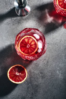 Koyu gri taşlı arka planda buz küpleri ve kan portakallı Negroni kokteyli..