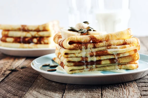 İnce gözlemeler, muzlu ve konsantre süt ahşap bir masada mavi bir tabakta..