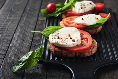 Açık sandviç veya mozzarella peynirli bruschetta, domates ve fesleğen, koyu ahşap arka planda Caprese..