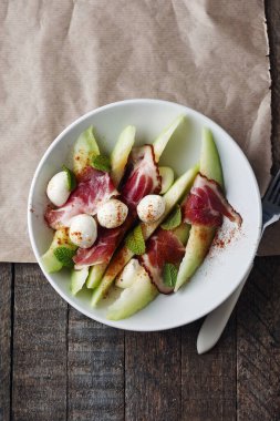 Melon with prosciutto, mozzarella balls and mint on a wooden background.