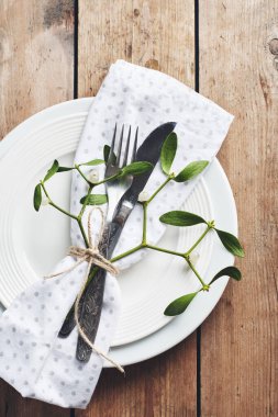 Masa ayarı. Beyaz tabak, çatal bıçak, peçete ve ökseotu..