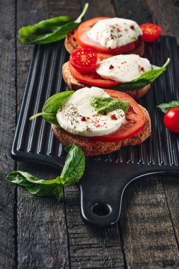 Açık sandviç veya mozzarella peynirli bruschetta, domates ve fesleğen, koyu ahşap arka planda Caprese..