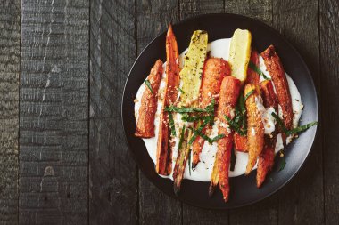 Yoğurtlu kızarmış havuç salatası, baharatlar ve siyah arka planda otlar..