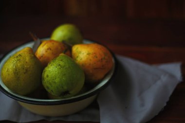 Ahşap bir tabakta su damlaları olan armutlar. Beyaz tavanda bir tabak armut. Siyah arka planda yeşil ve sarı armutlar. Armutları tabakta yıkadım.