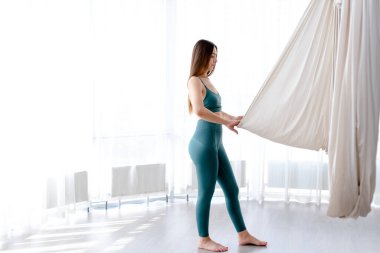 Güzel genç bir kadın hafif yoga stüdyosunda havacılık yogası için hamak çekiyor.. 