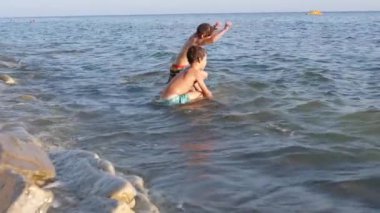 Sahilde, deniz dalgasında iki çocuk. Sörfte oynayan iki çocuk. Başıyla çocuğu saran dalgalar..