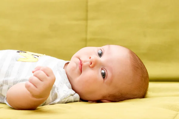 Baby lying on the green couch serious look — Stock Photo, Image