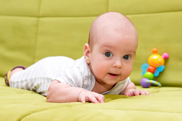 Baby liegt mit Spielzeug auf der grünen Couch — Stockfoto