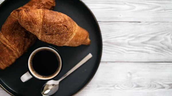 Taze pişmiş kruvasan ve sıcak bir kahve. Tahta masa üzerinde. Basit sabah kahvaltısı fotokopi alanı.